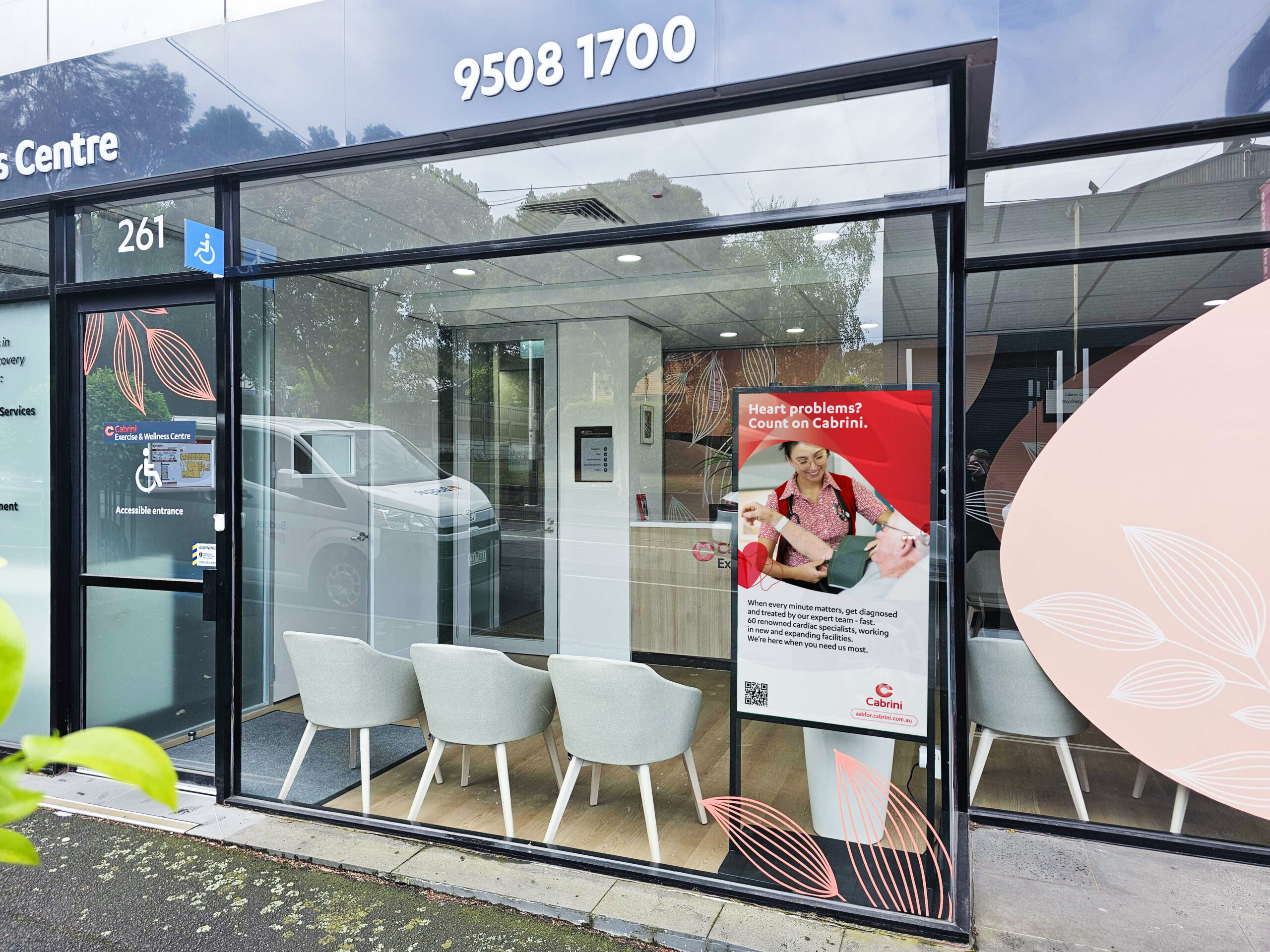 Accessible entrance sign with blue wheelchair icon on a glass storefront, row of seating inside a clinic. (Address 9508 1700 visible)