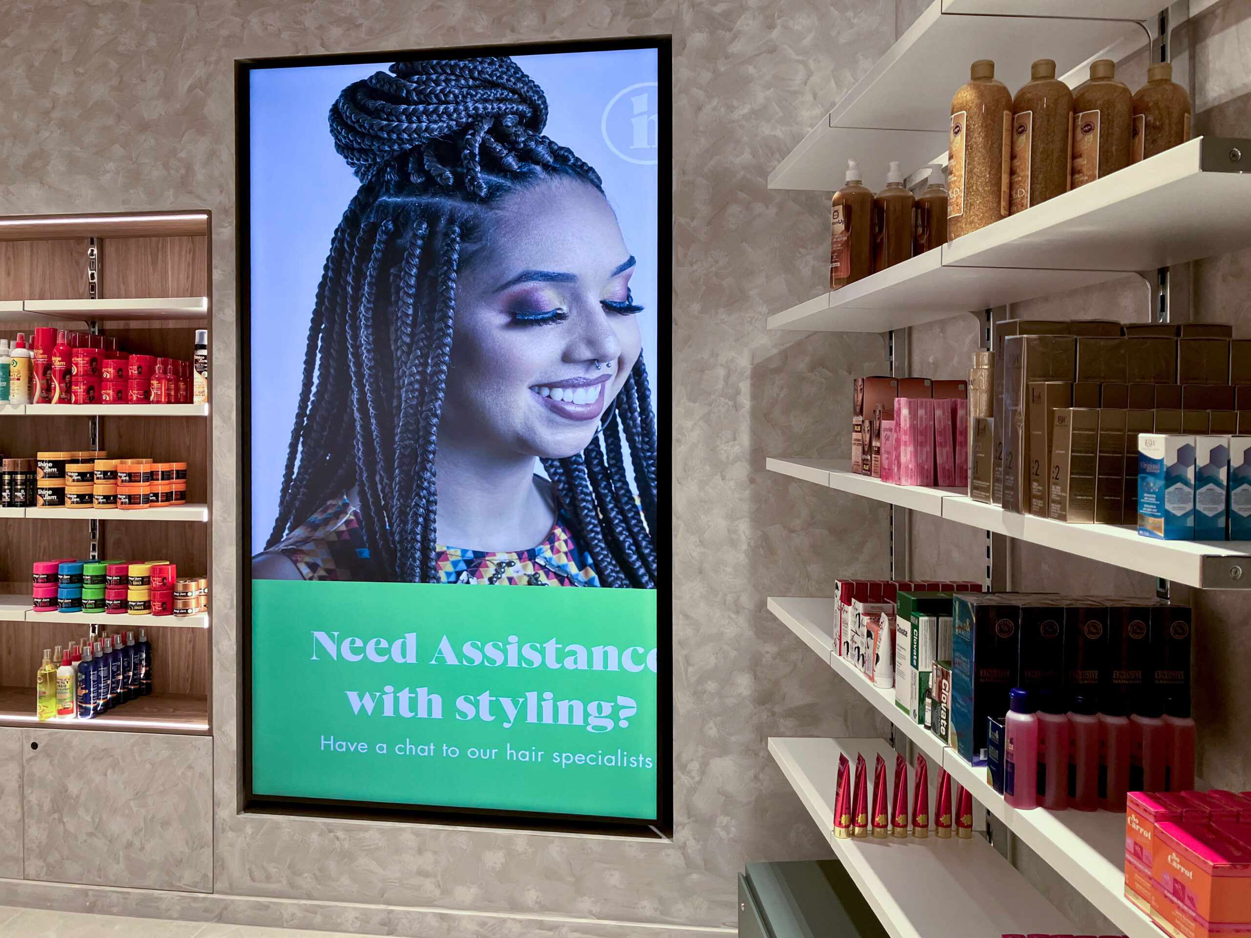 Large digital ad showing a smiling woman with braided hair in a beauty store, surrounded by hair products on shelves.