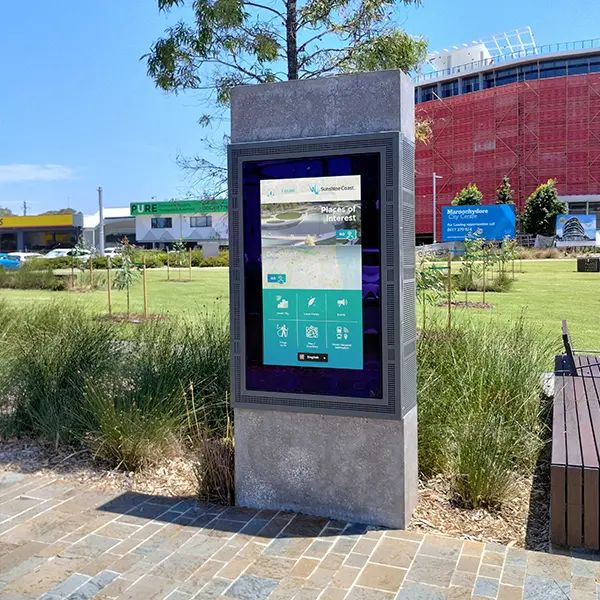 Public information touchscreen kiosk mounted in a stone pedestal in a park, displaying maps and local services in teal UI colors.