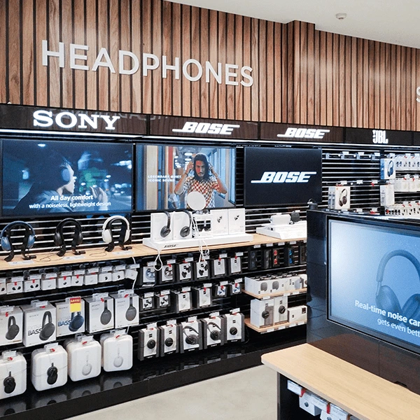In-store headphone display with Sony and Bose brands on a wooden wall backdrop in an electronics shop.