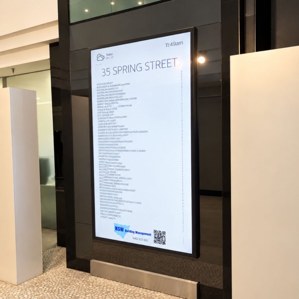 Tall digital directory display showing '35 Spring Street' with a long tenant list and NSW Building Management at the bottom, plus a QR code