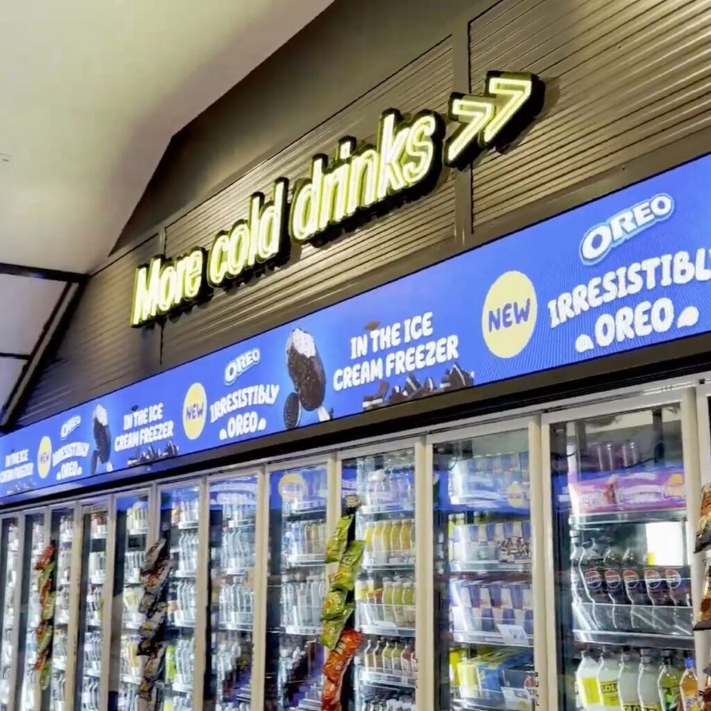 Storefront with a neon sign reading 'More cold drinks' above a row of refrigerated display cases.